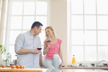 Happy couple looking at each other while drinking red wine in kitchen