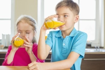 Siblings drinking orange juice in kitchen at home