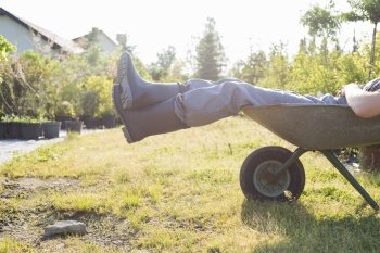 Low section of man relaxing in wheelbarrow at garden