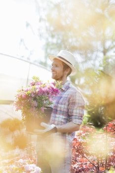 Smiling gardener looking away while holding flower pot outside greenhouse