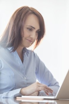 Mid-adult businesswoman using laptop at desk in office