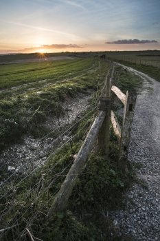 Beautiful Spring landscape of gate leading into fields with setting sun on horizon