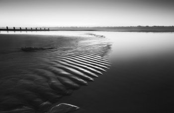 Beautiful low point of view along beach at low tide out to sea with vibrant sunrise sky in black and white