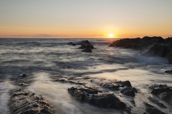Beautiful sunset landscape image of calm sea against rocky shoreline
