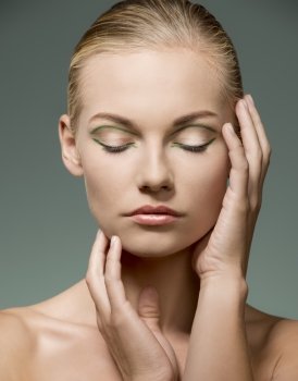 beauty shoot of sexy blonde woman with calm expression, naked shoulders, perfect visage skin and creative green make-up posing with hands near her face