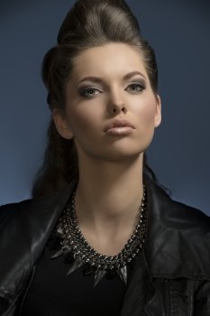 pretty girl posing in close-up fashion shoot with dark rock look and cute brown hair-style, wearing leather jacket and modern necklace looking in camera