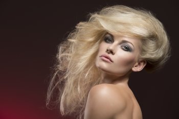 attractive blonde girl with fashion bushy creative hair-style posing with naked shoulders and cute make-up on red background. Looking in camera with charming expression 