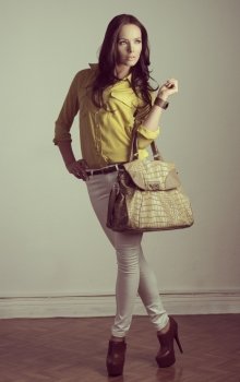 portrait of fashion brunette with modern casual style and natural hair-style. Wearing yellow shirt, white pants and taking cool bag in the hand