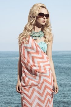 charming blonde girl posing in fashion shoot with summer look. Wearing sunglasses, pareo on bikini and turquoise necklace.