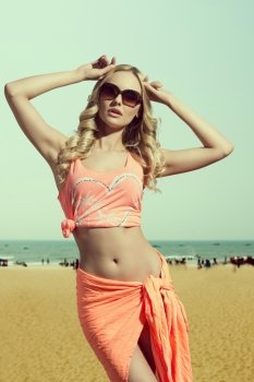 very sensual blonde female wearing orange pareo and sexy singlet in fashion pose with long shiny blonde hair 