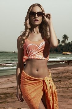 charming blonde lady with shiny wavy hair posing with orange pareo and sexy singlet in summer concept shot 