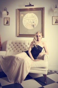 blond woman with hair style , in elegant interior , laying on white sofa and looking in camera