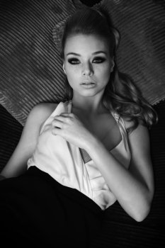black and white image , fashion portrait of elegant pretty lady , she has noce hair style , and she is looking in camera with her stunning eyes , laying on pillow