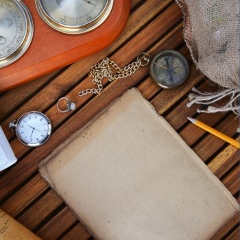 ancient mariner’s compass, watch and old paper on wooden background