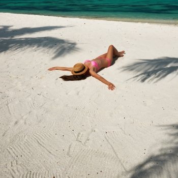 Woman in bikini at tropical beach under the palm tree shadow