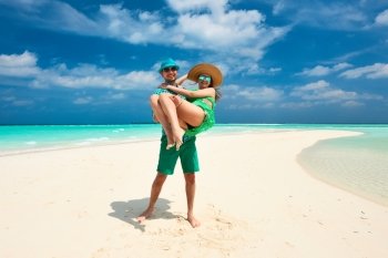 Couple in green on a tropical beach at Maldives. Man in holding woman on his arms.