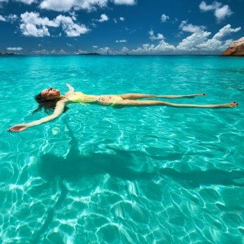 Woman in yellow bikini lying on water at tropical beach