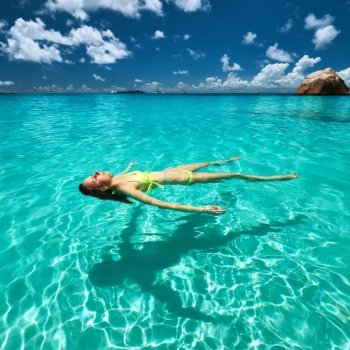 Woman in yellow bikini lying on water at tropical beach