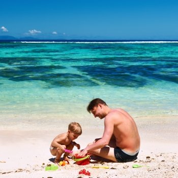 Two year old baby boy and his father playing on beach at Seychelles