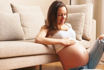 Pregnant woman at home sitting by the couch
