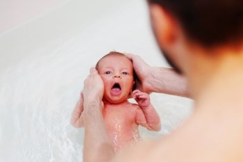 Newborn baby swimming in bath with help of father’s hands