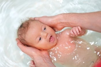 Newborn baby swimming in bath with help of father’s hands