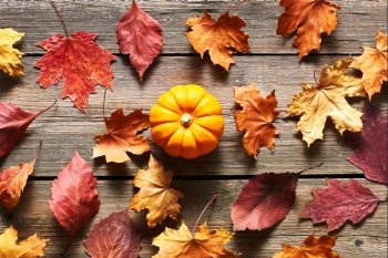 Autumn leaves and pumpkin over old wooden background 