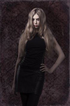 sexy young woman with mystery look and dark dress posing with long blonde hair and creative make-up. Halloween style 