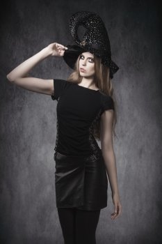 portrait of young blonde female in Halloween day posing with dark style, leather skirt, witch hat and creative make-up
