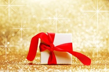 Christmas gift in white box with red ribbon decoration on golden background