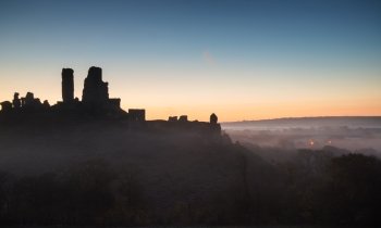 Vibrant sunrise over medieval castle ruins with fog in rural landscape