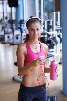 young healthy woman drinking water  in fitness gym while sitting on pilates ball and listening music on headphones from smartphone