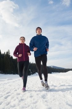 healthy young couple jogging outside on snow in forest. athlete running on  beautiful sunny winter day