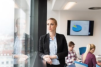 portrait of young business woman at modern startup office interior, team in meeting group in background