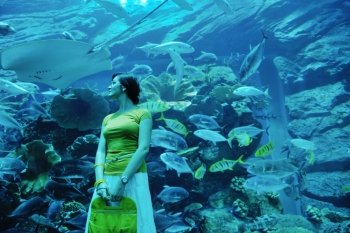 young woman  with big blue aquarium withmany  fish in background