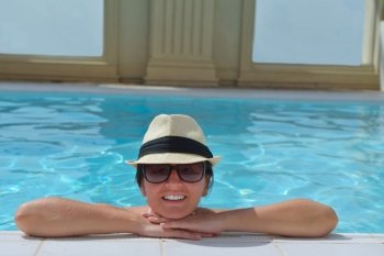Happy smiling woman with hat and sunglasses  in swimming pool at tropical resort