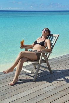 Beautiful young woman in bikini lying on a deckchair with a drink by the sea