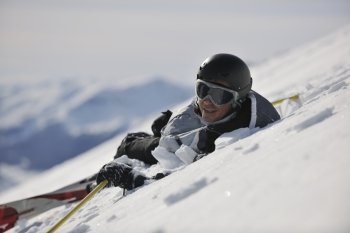 young skier relaxing in snow and looking mountain range at beautiful sunny winter day
