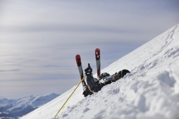 young skier relaxing in snow and looking mountain range at beautiful sunny winter day