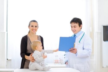 Interested baby reaches out to patients card in hand of pediatrician 

