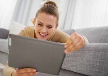 Smiling young woman using tablet pc while laying on sofa