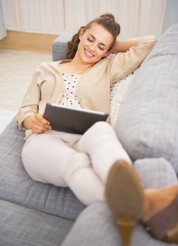 Happy young woman laying on divan and using tablet pc