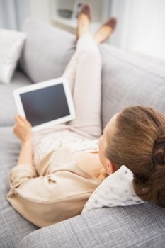 Young woman laying on couch with tablet pc . rear view