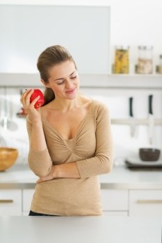 Thoughtful young housewife with apple in modern kitchen
