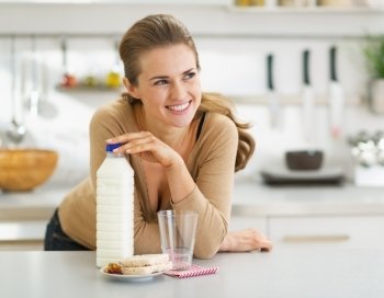 Thoughtful young woman with crisp bread and milk in modern kitchen