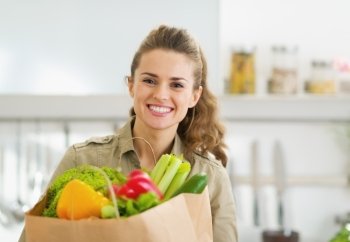Happy young housewife with shopping bag full of vegetables