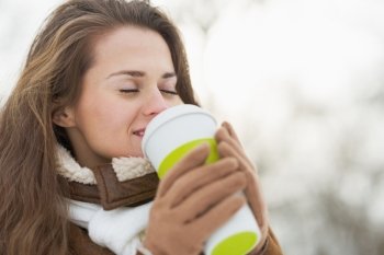 Happy young woman holding cup of hot beverage in winter outdoors