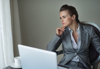 Thoughtful business woman working on laptop in hotel room