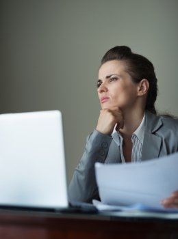 Thoughtful business woman working with documents and laptop at desk