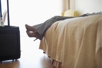 Closeup on legs of business woman laying on bed in hotel room after business trip